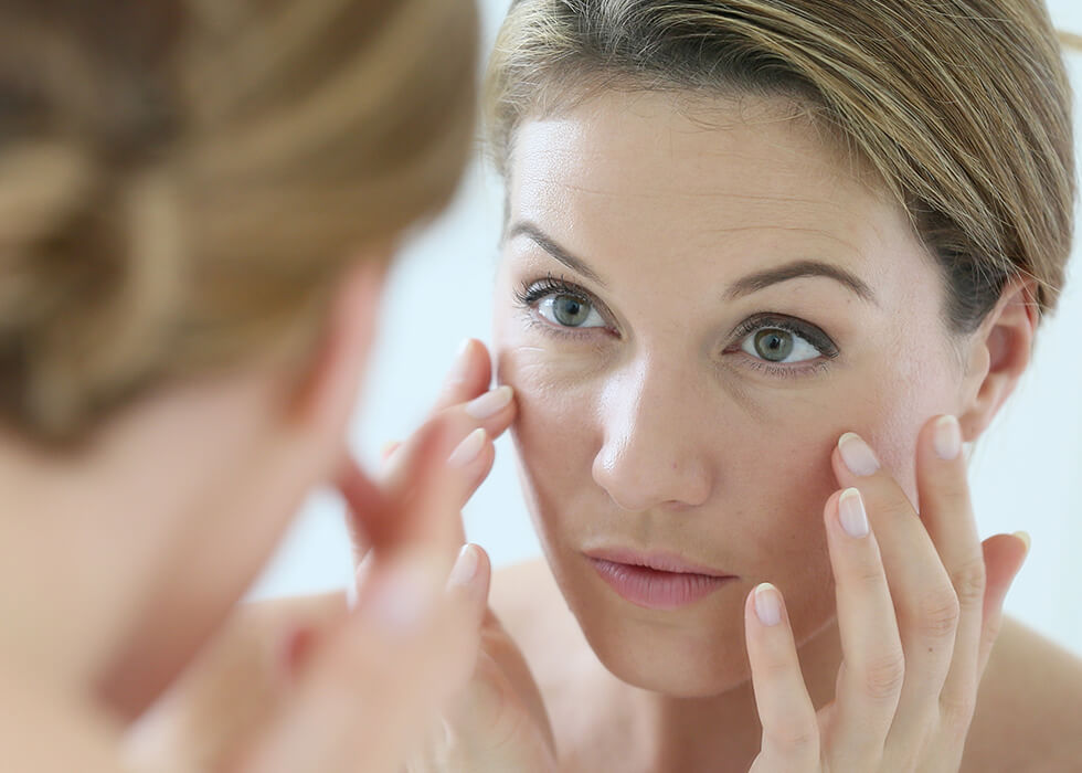 middle aged woman looking at aging skin in the mirror.